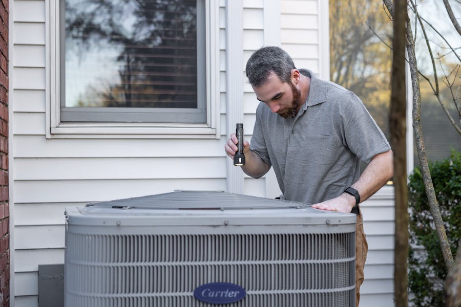 HVAC technician inspecting outdoor AC unit at residential property in Huntsville Alabama